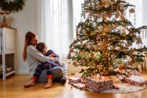 Мать и сын обнимаются у рождественской елки дома — стоковое фото