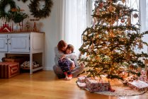 Mère et fils câlins par arbre de Noël à la maison — Photo de stock