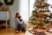 Madre e hijo abrazándose por el árbol de navidad en casa - foto de stock