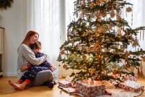 Mother and son hugging by christmas tree at home — Stock Photo