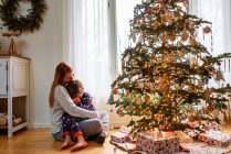 Мать и сын обнимаются у рождественской елки дома — стоковое фото