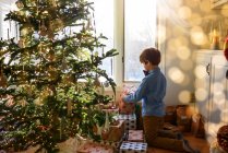 Boy kneeling in front of a Christmas tree looking at gifts — Stock Photo