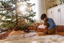 Menino ajoelhado na frente de uma árvore de Natal olhando para presentes — Fotografia de Stock