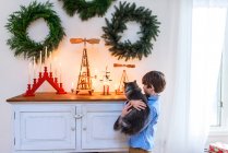 Хлопчик стоїть біля дошки з котом і дивиться на різдвяні прикраси. — стокове фото
