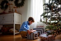 Ragazzo inginocchiato davanti a un albero di Natale a guardare regali — Foto stock