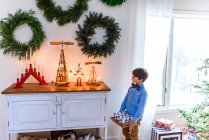 Junge steht an einem Sideboard mit Geschenken und schaut sich Weihnachtsdekoration an — Stockfoto