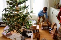 Junge steht am Weihnachtsbaum und betrachtet Geschenke — Stockfoto