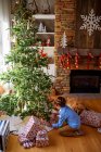Junge kniet vor Weihnachtsbaum und betrachtet Geschenke — Stockfoto