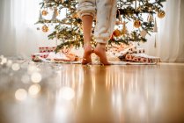 Primer plano de las piernas de una chica de pie junto a un árbol de Navidad - foto de stock