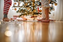 Primer plano de las piernas de dos niños mientras decoran un árbol de Navidad - foto de stock