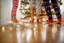 Close-up of three children's legs while decorating a Christmas tree — Stock Photo