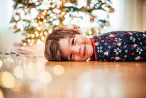 Smiling boy lying on the floor in front of a Christmas tree — Stock Photo
