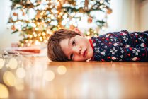 Мальчик лежит на полу перед елкой — стоковое фото