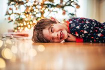 Junge liegt lachend auf dem Boden vor Weihnachtsbaum — Stockfoto