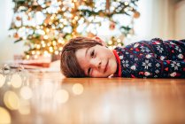 Улыбающийся мальчик лежит на полу перед елкой — стоковое фото