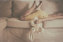 Garçon couché sur un canapé tenant un jouet doux — Photo de stock