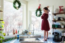 Sonriente chica de pie en una encimera de cocina poniendo decoraciones de Navidad - foto de stock