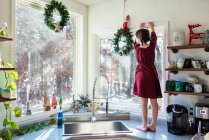 Chica de pie en una encimera de cocina poniendo decoraciones de Navidad - foto de stock
