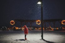 Девушка, стоящая в снегу, глядя на уличный фонарь, США — стоковое фото