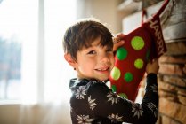Sonriente niño colgando una media de Navidad en una chimenea - foto de stock