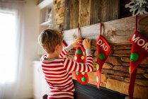 Menino pendurado uma meia de Natal em uma lareira — Fotografia de Stock