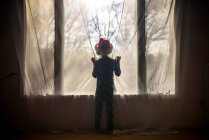 Garçon portant un chapeau de Père Noël regardant par une fenêtre — Photo de stock