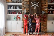 Three children hanging up Christmas stockings on a fireplace — Stock Photo