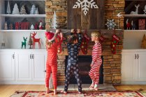 Trois enfants accrochent des bas de Noël sur une cheminée — Photo de stock