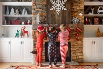 Drei Kinder hängen Weihnachtsstrümpfe am Kamin auf — Stockfoto