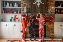 Three children hanging up Christmas stockings on a fireplace — Stock Photo