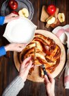 Mujeres rebanando canela recién horneada y manzana Brioche guirnalda dulce - foto de stock