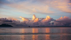 Belo céu por do sol refletindo na água do mar com rochas distantes — Fotografia de Stock