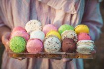 Female hand holding tray with colorful sweet macaroons on table, close view — Stock Photo