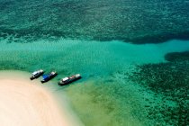 Vista elevada de tres barcos en el agua en laguna azul por playa de arena - foto de stock