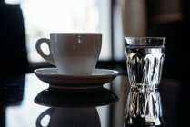 Gros plan d'une tasse de café et d'un verre d'eau sur une table — Photo de stock