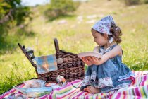 Улыбающаяся девушка, сидящая на одеяле для пикника в парке и решающая, какую еду есть, Болгария — стоковое фото