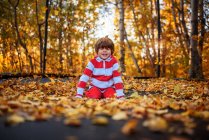 Sonriente Niño sentado en un trampolín cubierto de hojas de otoño, Estados Unidos - foto de stock