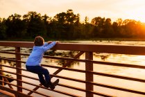 Хлопчик, що вилазить на поручні моста на заході сонця (США). — стокове фото