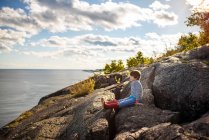 Boy sitting on rocks by a lake, Lake Superior Provincial Park, Estados Unidos — Fotografia de Stock