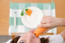Overhead view of a girl sitting at a table eating a carrot — Stock Photo