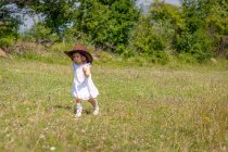 Mädchen im Sommerkleid und Cowboyhut läuft auf einer Wiese, Bulgarien — Stockfoto