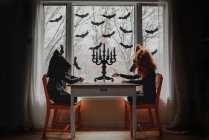 Duas crianças em trajes de Halloween sentadas perto de uma janela fazendo um quebra-cabeça, Estados Unidos — Fotografia de Stock