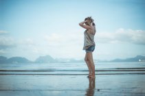 Side view of a woman standing on the beach putting her hair in a pony tail, Koh Yao, Phang Nga, Thailand — Stock Photo