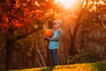 Хлопець стоїть у саду з гарбузом (США). — стокове фото