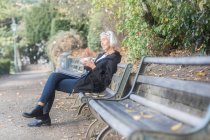 Mulher sênior sentado no banco do parque com xícara de café — Fotografia de Stock