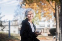 Mujer sonriente sentada en el parque con una taza de café - foto de stock