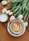 Cup of coffee on a table with a bunch of tulips and a candle — Stock Photo