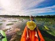 Niño en kayak sosteniendo flor de lirio en la escena del lago - foto de stock