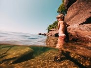 Boy standing in a lake holding onto rocks, Lake Superior, Estados Unidos - foto de stock