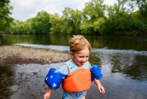 Улыбающийся мальчик в спасательной рубашке, бегущий вдоль берега реки, США — стоковое фото